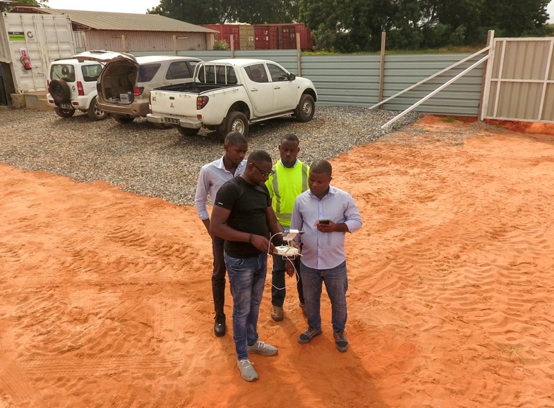 Angola Flying Labs - 4 men huddled around a drone flight controller